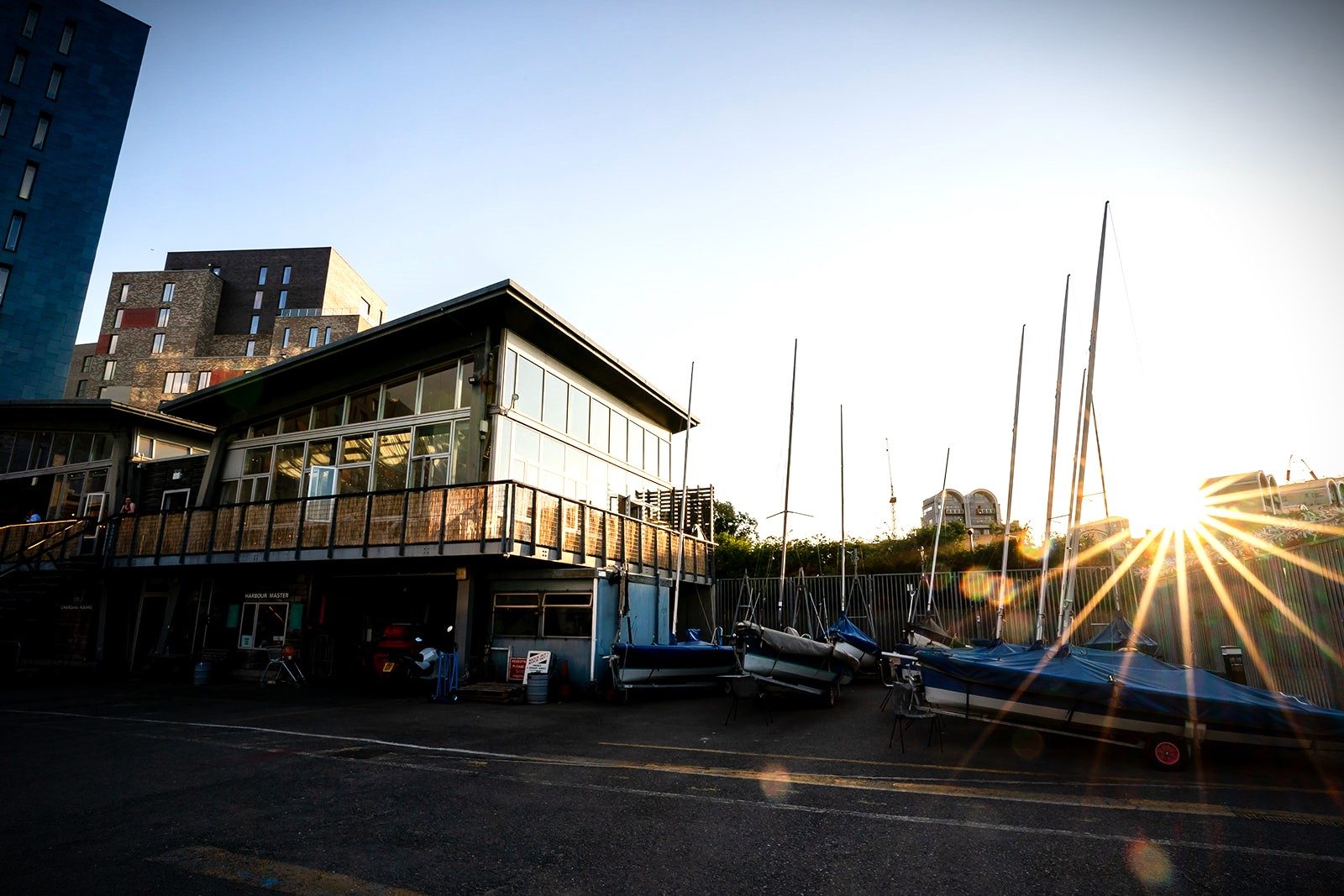 The clubhouse from the yard at sunset, the sun flaring behind a row of dinghy masts