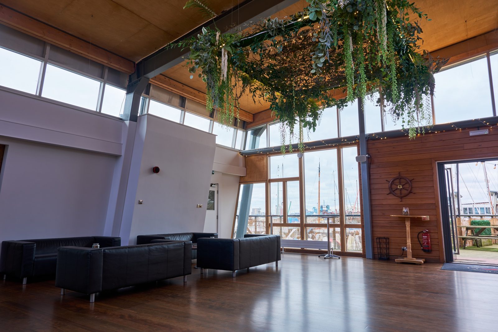 Black leather sofas in the clubhouse function room with greenery hanging from the beams and masts visible through the glass