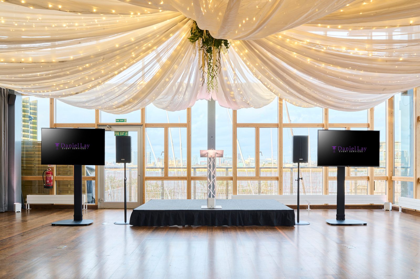 A small stage with two screens set up under the draped ceiling of the River Rooms for a conference