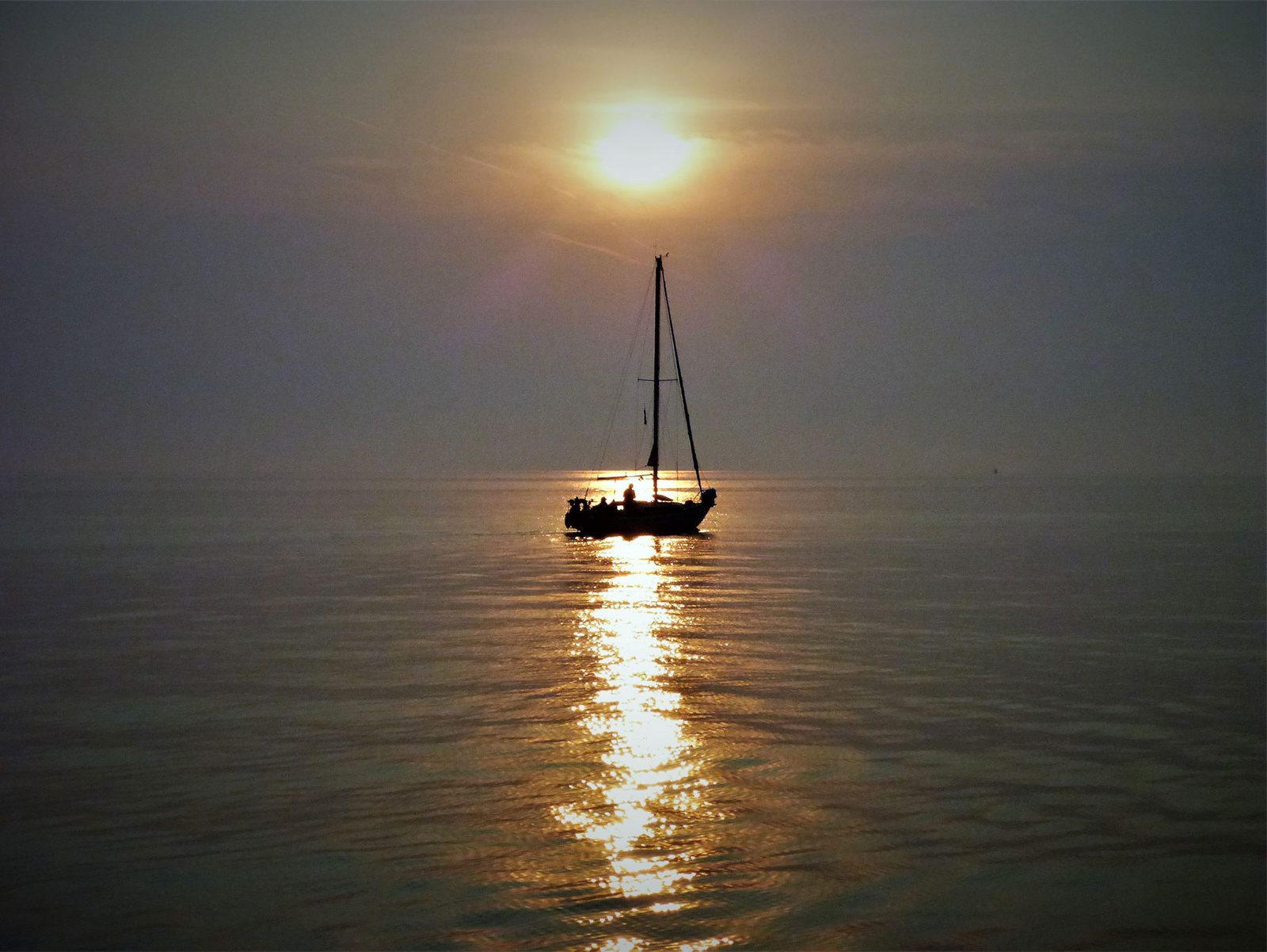 A yacht at anchor silhouetted against the setting sun on flat calm water