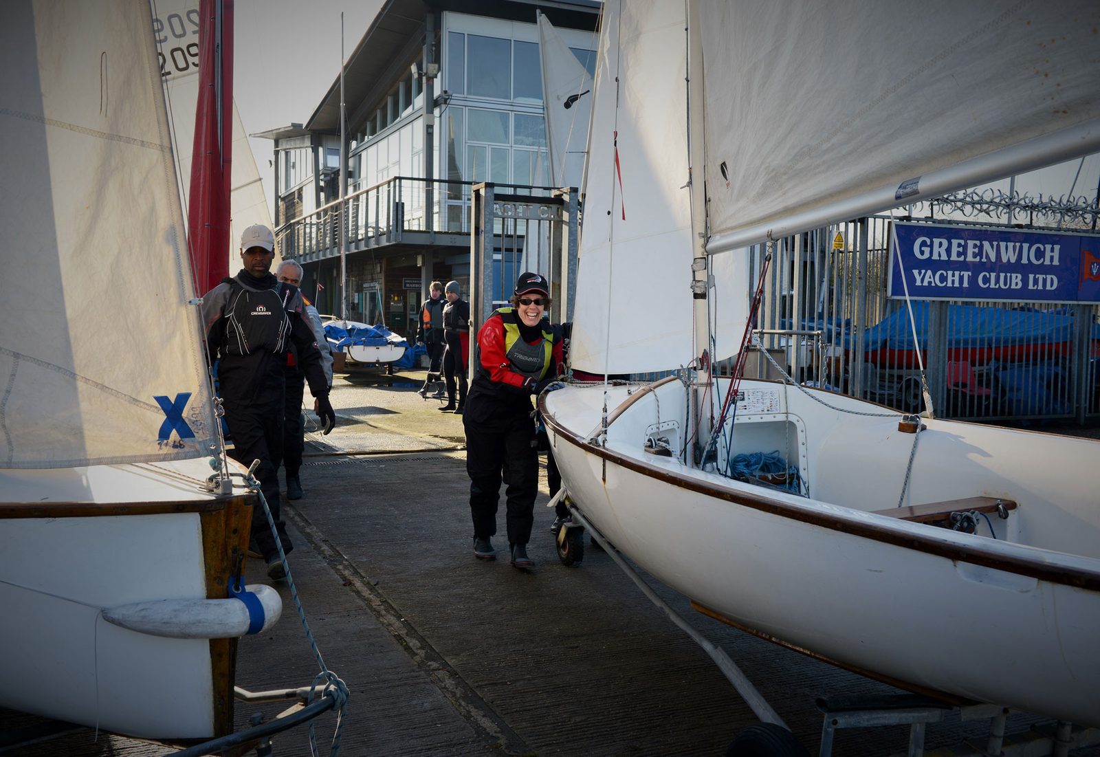 Members wheeling a Wayfarer down the slipway to launch, sails up, with the clubhouse behind