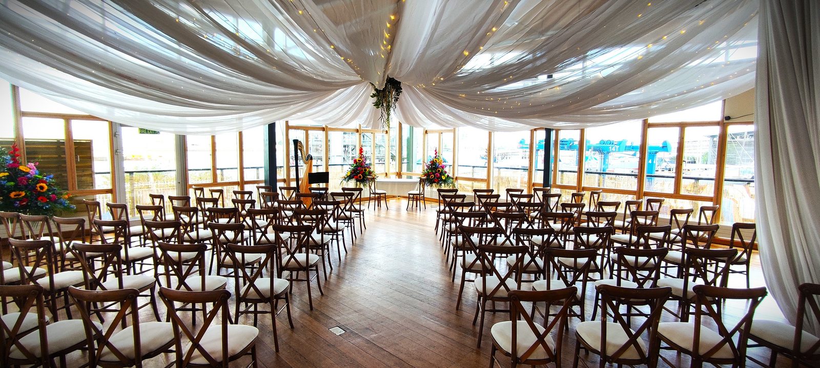 Round tables with white cloths and crossback chairs laid for a wedding breakfast in the River Rooms