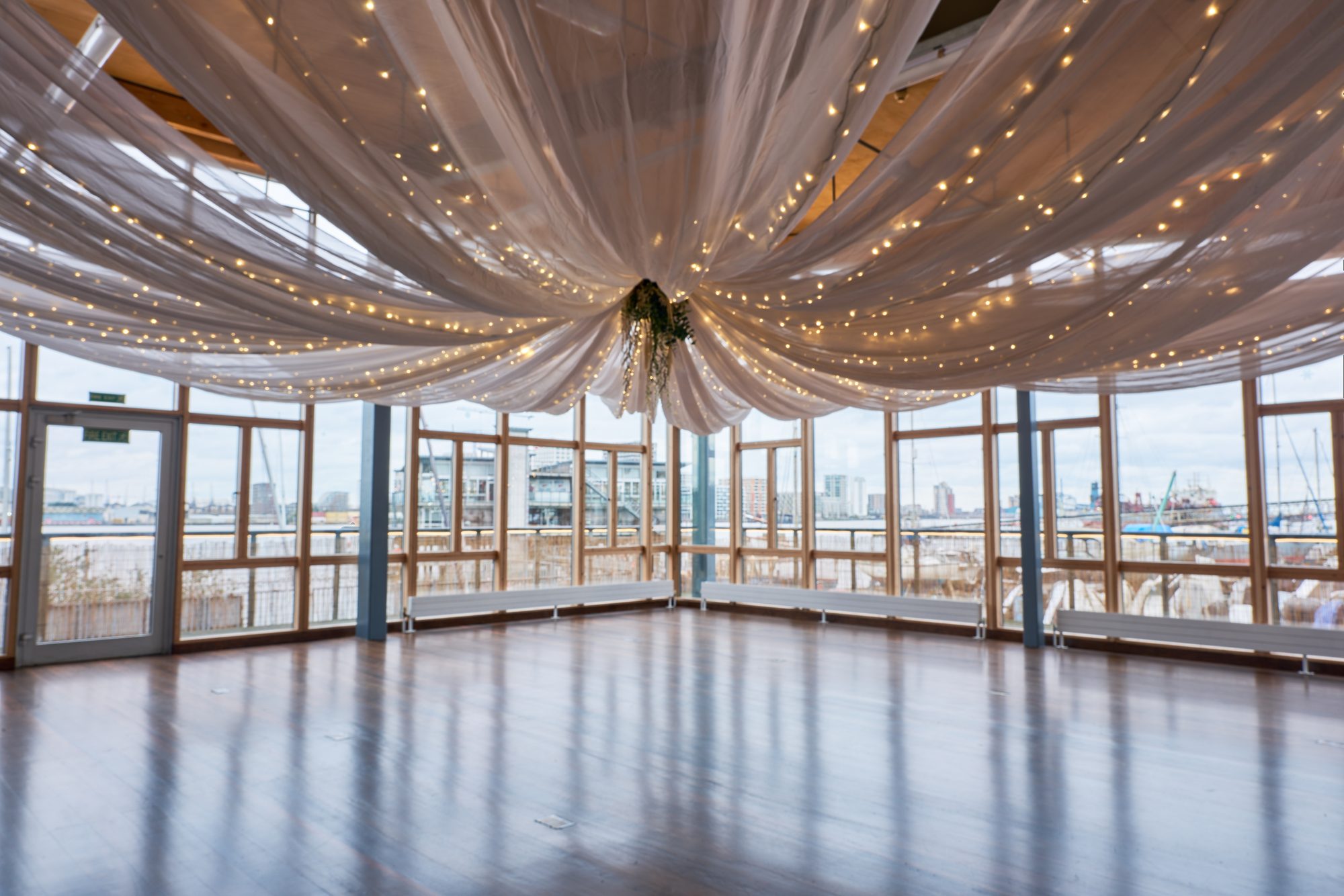 The River Rooms empty with a white draped ceiling and fairy lights, windows on three sides looking over the Thames