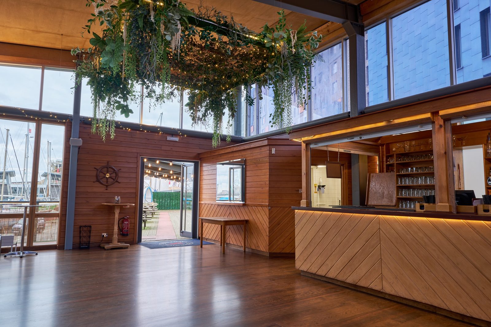 Wood panelled lounge end of the River Rooms with the bar, black leather sofas and greenery on the beams