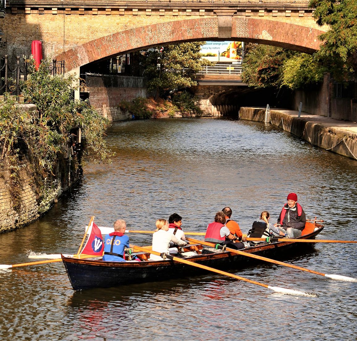 A club cutter rowing under a brick bridge on a tree lined creek off the Thames