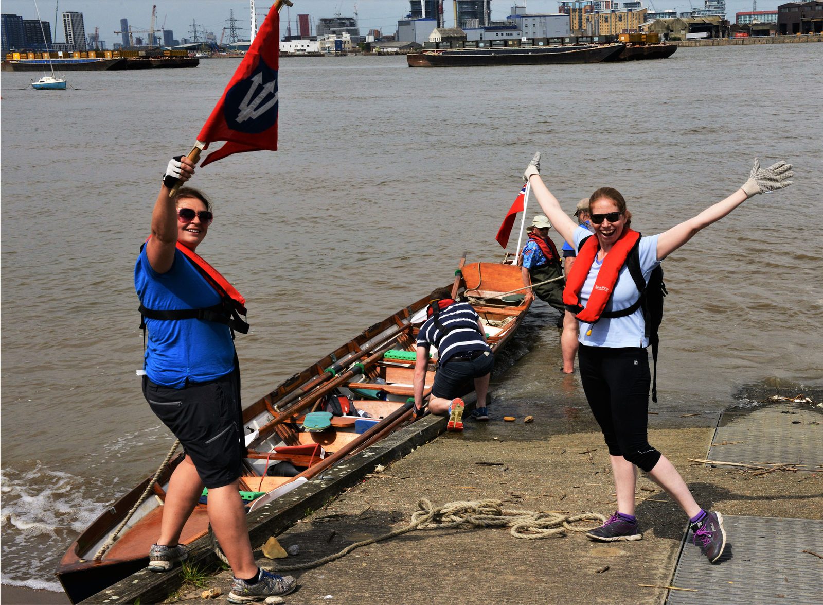 Two rowers celebrating on the foreshore with the club burgee, the cutter behind them