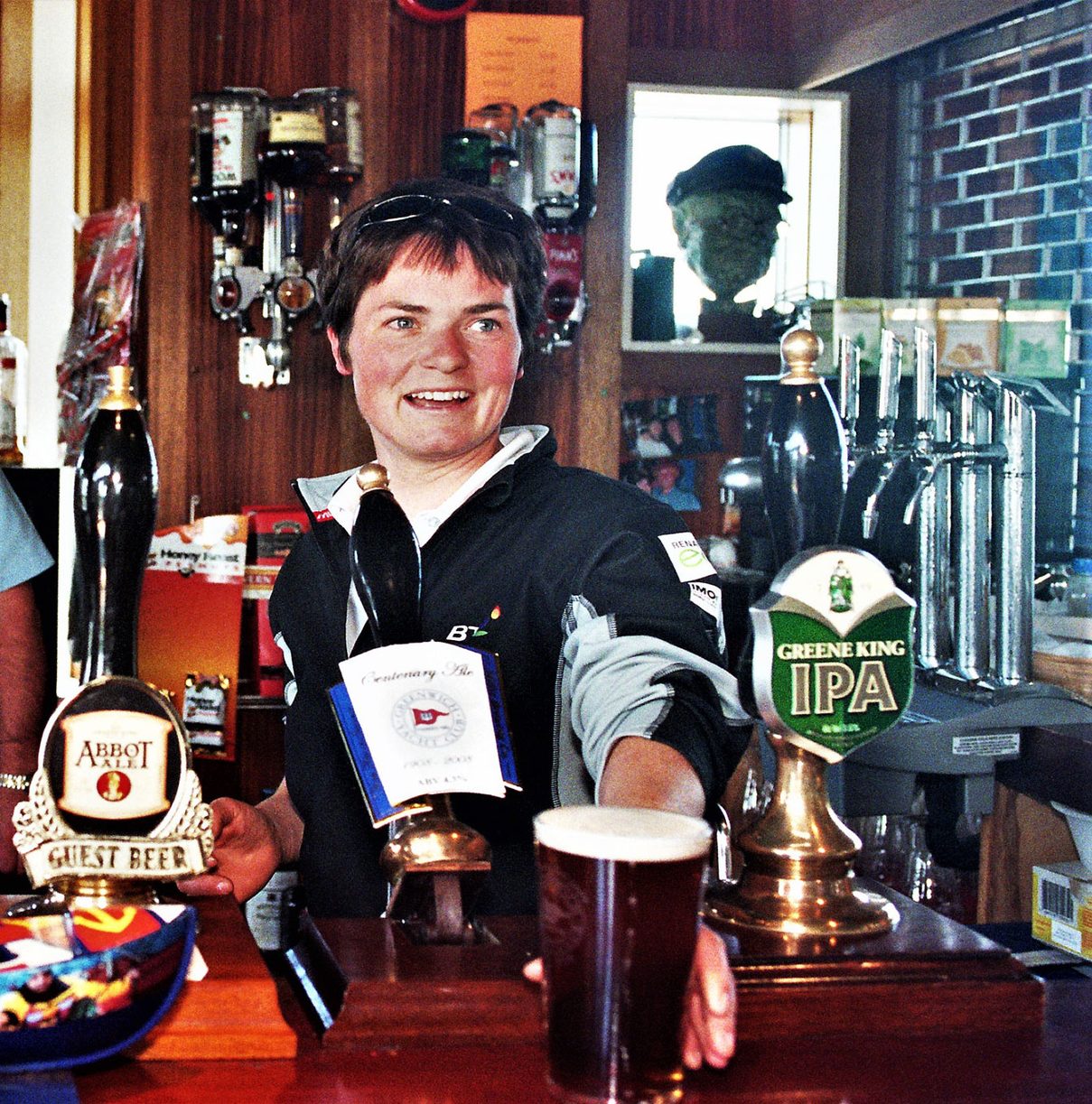A member behind the clubhouse bar with a pint on the counter and the pumps and optics behind