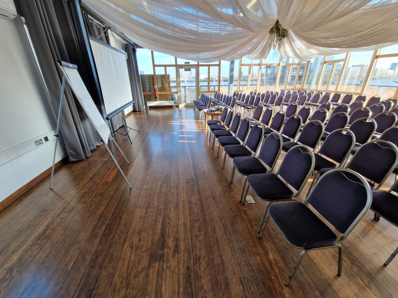 Rows of navy conference chairs set out theatre style facing a projector screen, with the river beyond the windows