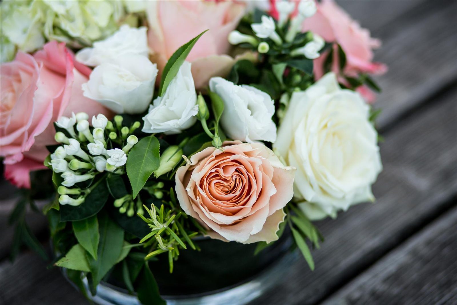 A bridal bouquet of peach, pink and white roses on a wooden table