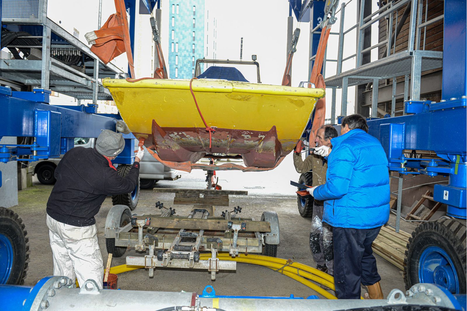 A yellow hulled dinghy in the yard hoist being lowered onto its trailer