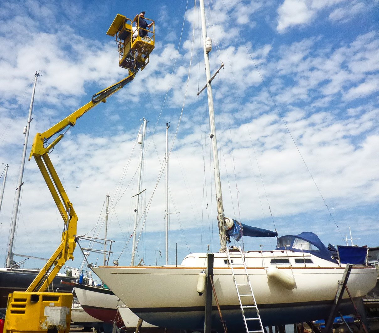 The yard crane lifting a yacht out of the water, masts against a blue sky